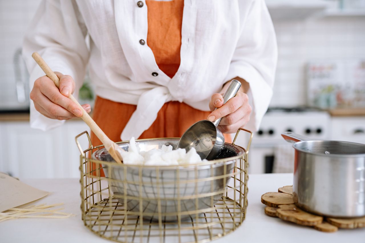 A person making homemade candles using soy wax in a warm kitchen setting.